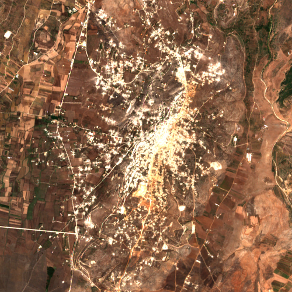 The same view on 16 September 2026: the town centre and the ground south of it look paler and more mottled, with orange-brown patches along a line to the south; the fields to the west are darker and more uniform.